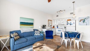 Ein modernes Wohnzimmer mit einem blauen Sofa, einem runden Couchtisch und einer Küchenzeile mit weißen Schränken sowie einem Esstisch.