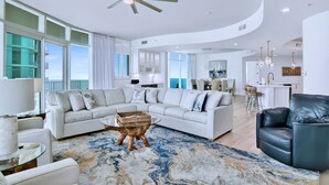 A spacious living room with a large sectional sofa, a glass coffee table, and a modern ceiling fan.
