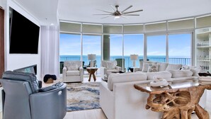 A spacious living room with a large window overlooking the ocean, a ceiling fan, and a modern coffee table.