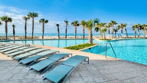 A pool area with lounge chairs and palm trees, overlooking a beach.