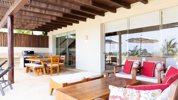 Un espacio de patio al aire libre con mobiliario de madera, una parrilla y vistas al océano.