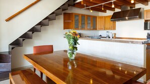 Cocina moderna con armarios de madera, campana extractora de acero inoxidable y comedor con mesa y banco de madera.