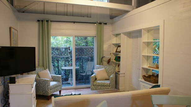 Una sala de estar con televisión, dos sillones estampados, un sofá y un ventanal corredero que da a un patio.