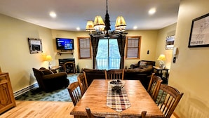 A dining area with a wooden table and chairs, a chandelier, and a television in the background. - Lake Placid Pinehill Townhome, Your "Next Adventure" vacation (Lake Placid)