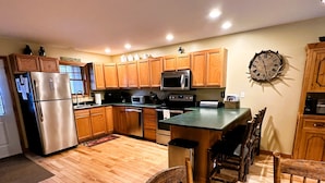 A modern kitchen with wooden cabinets, stainless steel appliances, and a dining area with a wooden table and chairs. - Lake Placid Pinehill Townhome, Your "Next Adventure" vacation (Lake Placid)