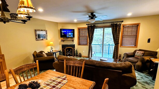 A cozy living room with a fireplace, a television, and a dining area with a wooden table and chairs. - Lake Placid Pinehill Townhome, Your "Next Adventure" vacation (Lake Placid)