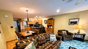 A cozy living room with a sofa, a dining table, and chairs. There is a kitchen area with wooden cabinets and a microwave. - Lake Placid Pinehill Townhome, Your "Next Adventure" vacation (Lake Placid)