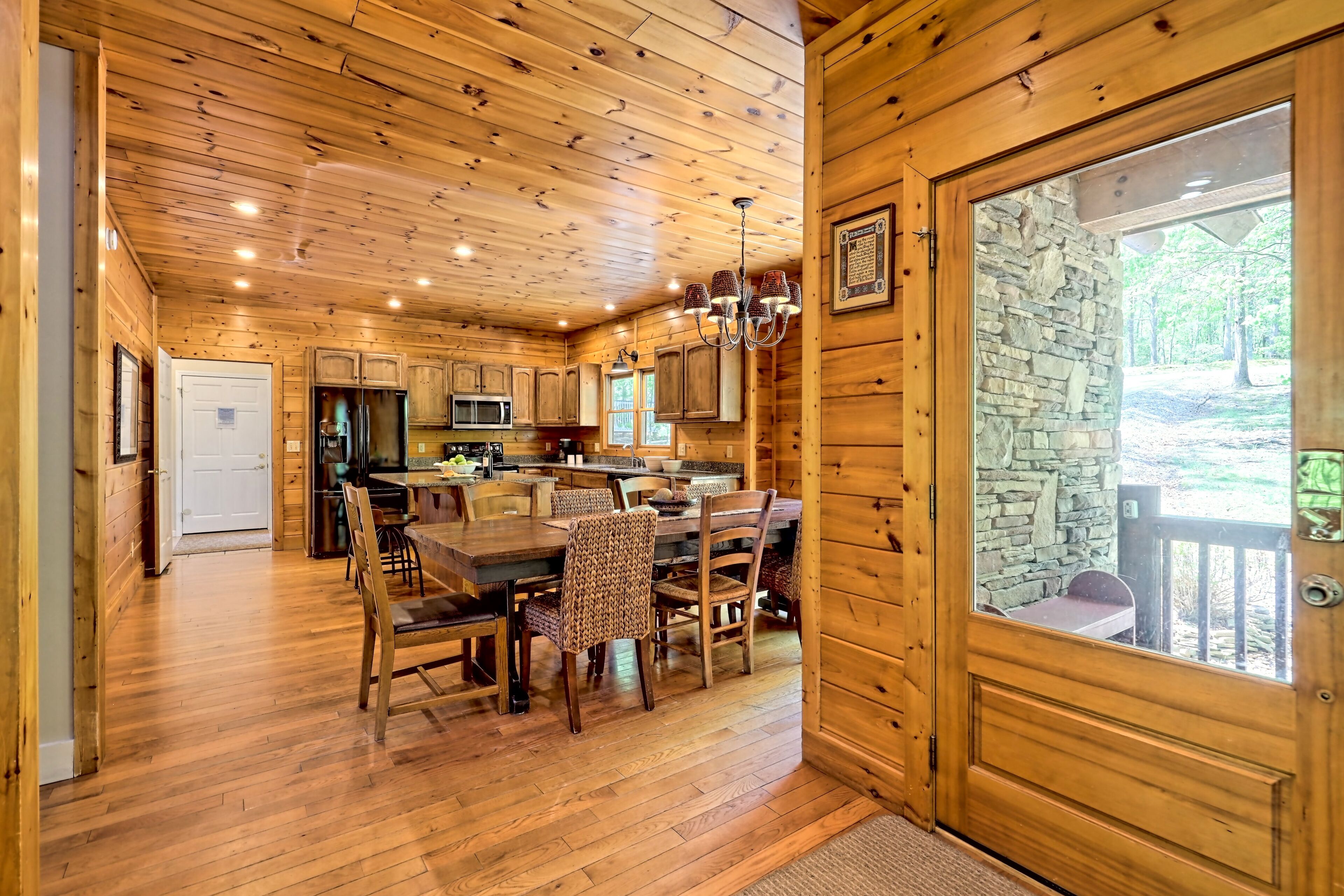 A wooden cabin interior with a dining area, kitchen, and a stone wall door.