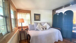 Quarto com cama, mesa de cabeceira, luminária e janela com cortinas.