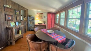 Uma área de refeições com uma mesa e cadeiras de madeira, uma estante e uma janela com cortinas.