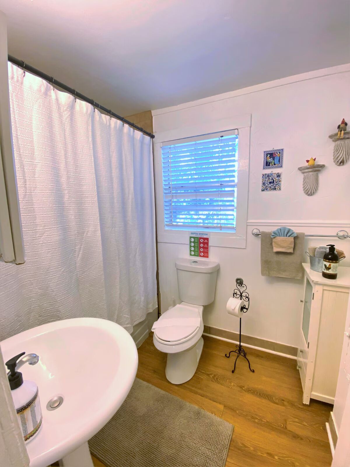 A compact bathroom with a toilet, sink, and window with blinds.