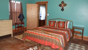 Een slaapkamer met een bed, een plafondventilator, een houten deur, een kruis aan de muur, en een raam met gordijnen.