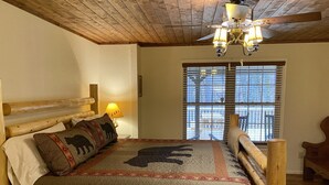 Una cama con estructura de madera, un edredón acolchado, una lámpara de noche y una ventana con persianas.
