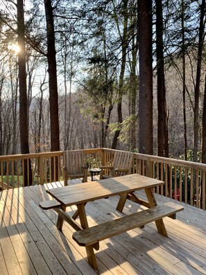 A wooden deck with a picnic table and chairs, surrounded by trees.