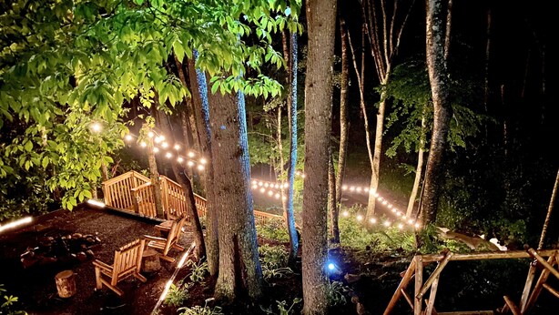 Una terraza de madera con un pequeño estanque, rodeada de árboles y luces colgantes.