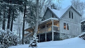 Una cabaña de madera con balcón, rodeada de árboles cubiertos de nieve.