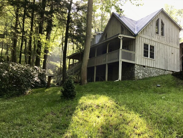 A wooden cabin with a porch, surrounded by trees and grass.