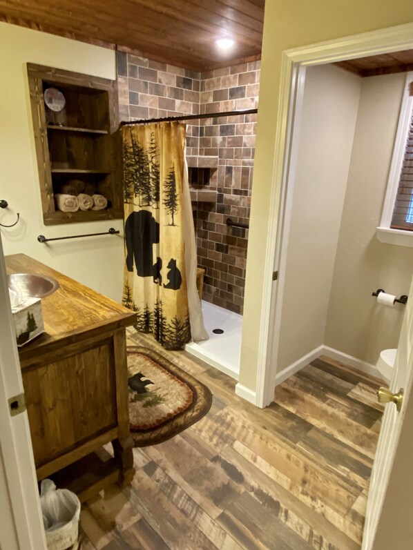 A bathroom with a shower, a wooden vanity, a towel rack, and a window.