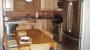 Une cuisine compacte avec des meubles en bois, un réfrigérateur en acier inoxydable, un lave-vaisselle et une table à manger avec des chaises.