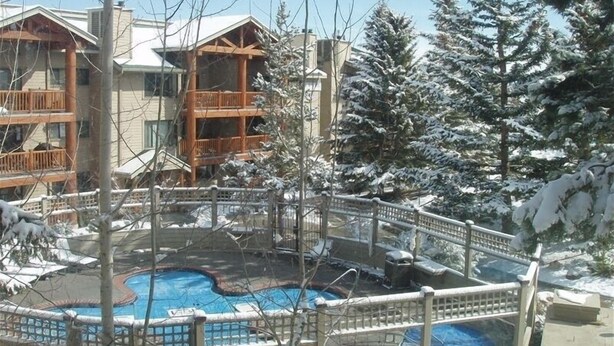 Un complexe hôtelier doté d’une piscine entourée d’arbres couverts de neige et d’un bâtiment en bois agrémenté de balcons.