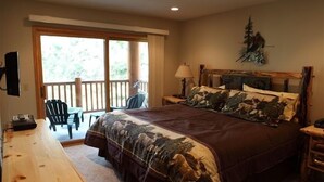 Une chambre avec un grand lit, un bureau en bois, une chaise, une table de chevet, une lampe et une vue sur l’extérieur grâce à une porte-fenêtre coulissante.