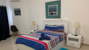 A neatly arranged bedroom with a bed, bedside tables, a chair, and a view of the outside through a window.