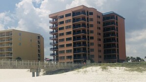 A beachfront hotel with multiple floors, balconies, and a sandy beach in the foreground.