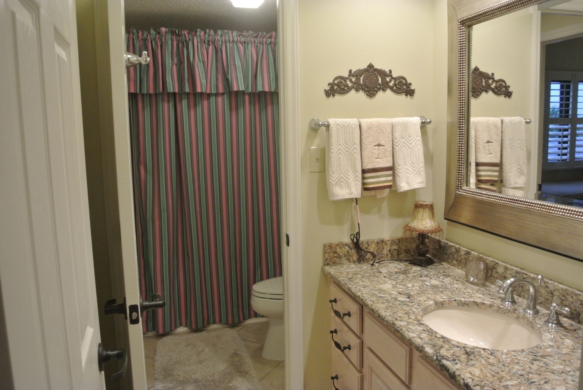 A bathroom with a striped shower curtain, a sink with a marble countertop, and a mirror with a decorative frame.