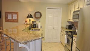 A kitchen with granite countertops, white cabinetry, a double door, a refrigerator, a stove, and a coffee maker.