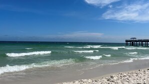 A beach with waves, a pier, and a clear sky.
