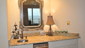 A kitchen with a granite countertop, a sink, a mirror, a ceiling fan, and a window with a view of the ocean.