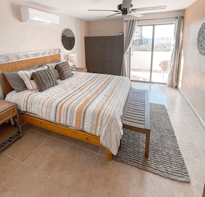 Une chambre à coucher comprenant un lit, une table de chevet, un ventilateur de plafond, une fenêtre avec des rideaux et une vue sur l’extérieur.