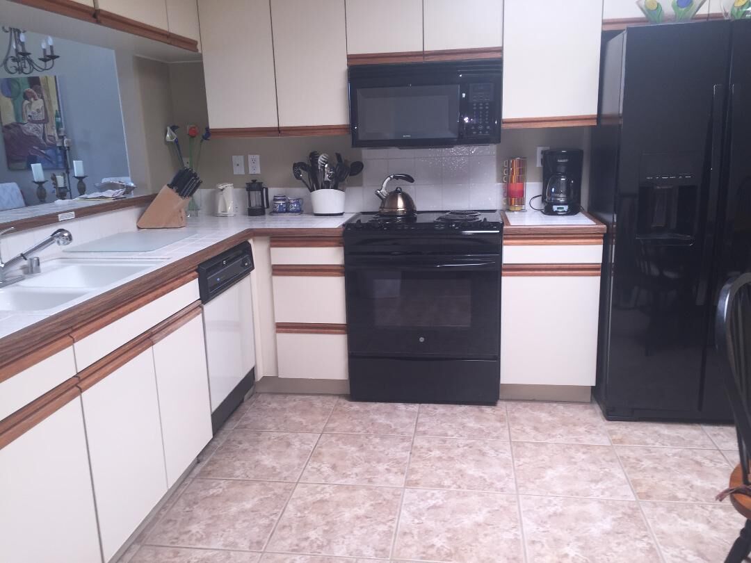 Une cuisine avec des meubles blancs, une cuisinière noire, un four à micro-ondes et un réfrigérateur.