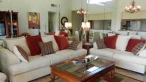 A spacious living room with a large mirror, white sofas with red and striped cushions, a wooden coffee table, and a chandelier. - BEAUTIFUL SUNRISES.  THREE MASTER SUITES (Palm Desert)
