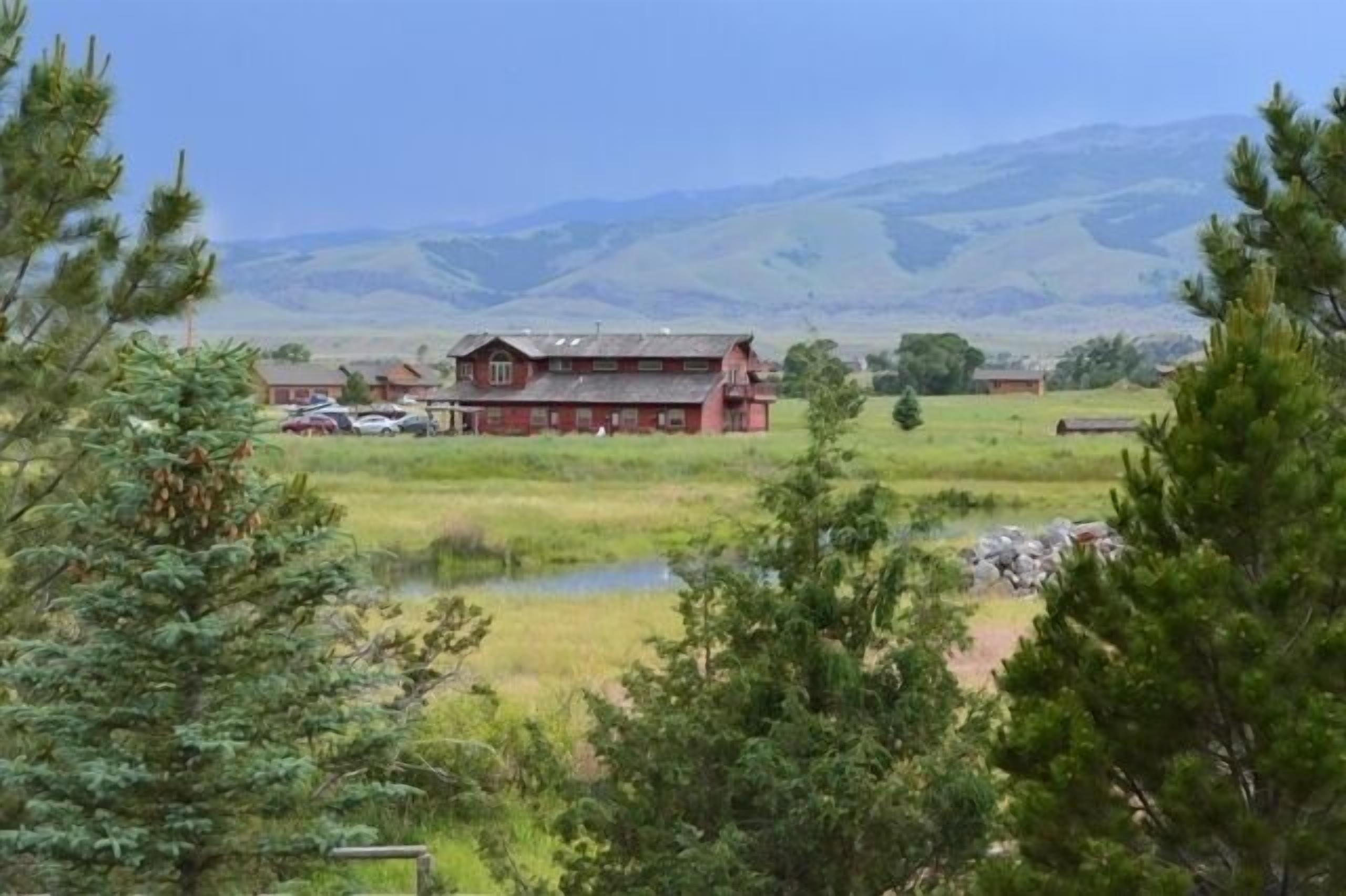 A red barn with a large porch, surrounded by open fields and distant mountains.
