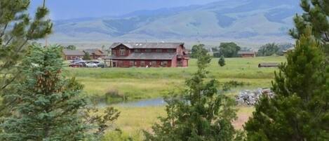 A red barn with a large porch, surrounded by open fields and distant mountains.