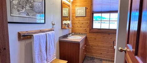 A bathroom with wooden walls, a sink, a bench, and a framed picture on the wall.