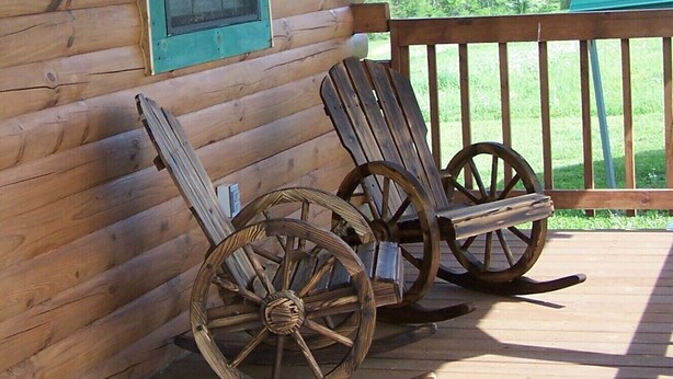 Two rocking chairs on a wooden deck with a wooden cabin wall in the background.