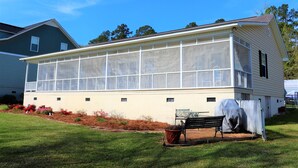 A house with a large glass extension, a covered bench, and a garden area with flowers. - Lakefront Cottage on Lake Marion (Summerton)