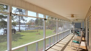 A covered porch with large windows overlooking a grassy area and a dock. - Lakefront Cottage on Lake Marion (Summerton)