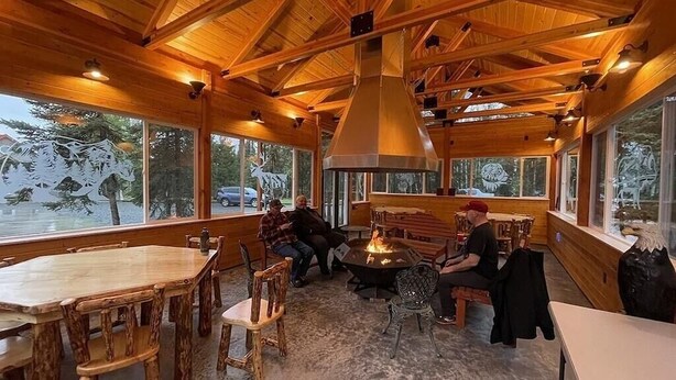 A wooden interior with a high ceiling, large windows, a central fire pit, and seating areas. - Prime Kenai River Frontage with Private Lodging (Sterling)