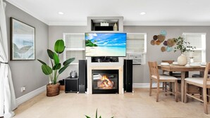 A modern living room with a fireplace, a flat-screen TV, and a dining area. - Steps from Beach: Stylish Getaway (Newport Beach)