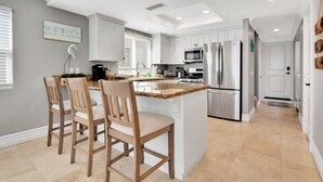 A modern kitchen with white cabinets, a central island with bar stools, stainless steel appliances, and a 'RELEASE' sign on the wall. - Steps from Beach: Stylish Getaway (Newport Beach)