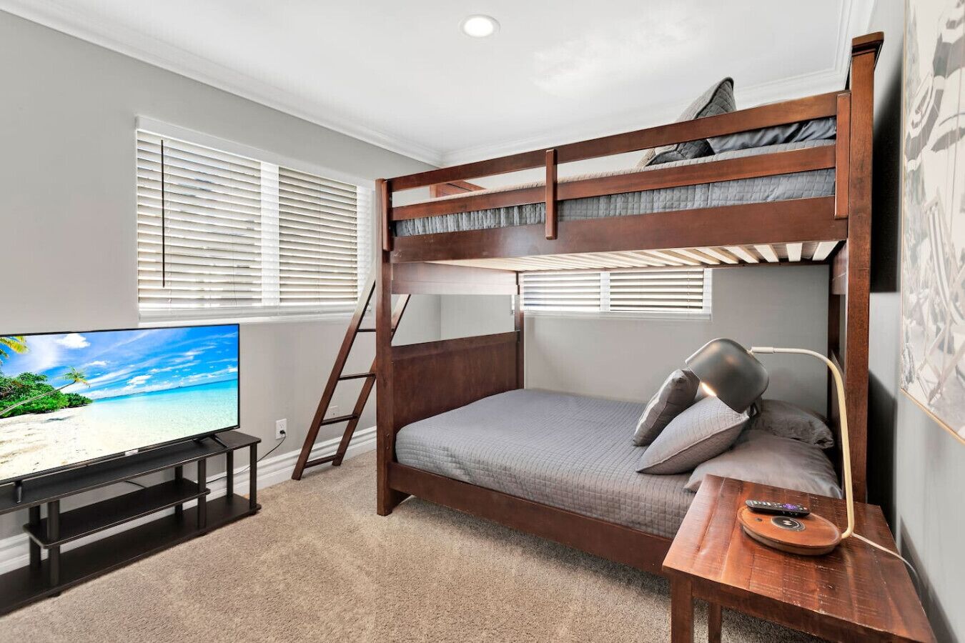 Une chambre avec un lit superposé, une télévision, une échelle et un bureau équipé d’une lampe et d’une télécommande.