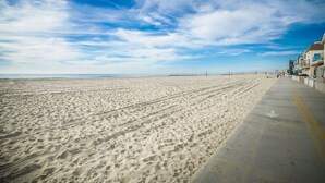 A wide sandy beach with a concrete walkway on the right, leading to buildings. - Steps from Beach: Stylish Getaway (Newport Beach)