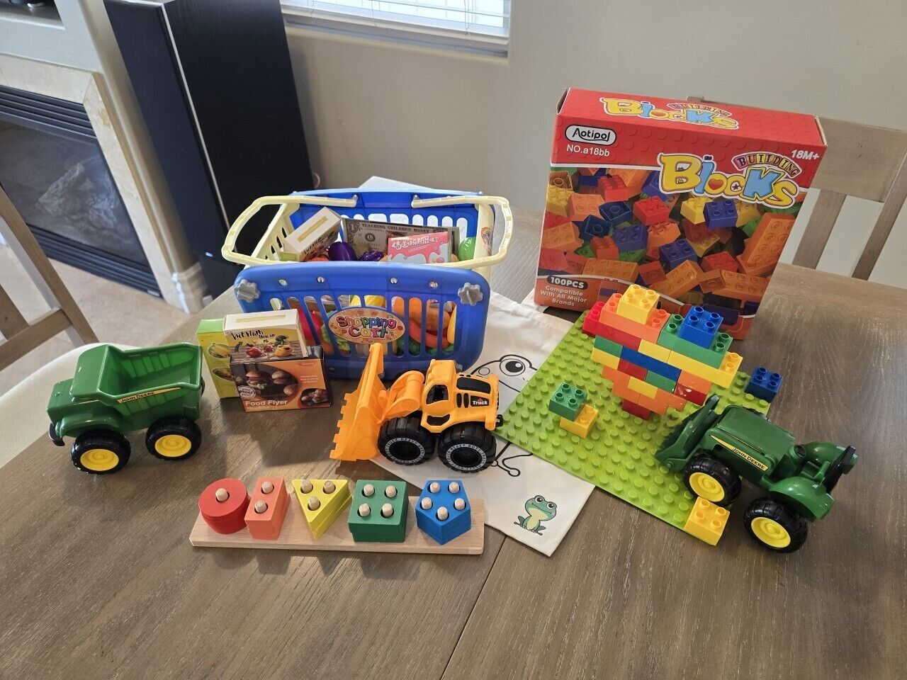 Una mesa con varios juguetes y bloques de construcción, incluyendo un camión volquete verde, una excavadora de juguete y un set de LEGO.