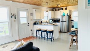 A modern kitchen with white cabinets, a stainless steel refrigerator, and a central island with stools. - Oceanfront Jewel Getaway! PEI oceanfront cottage just minutes from Cavendish. (New London)