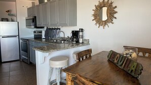 Een keuken met grijze kastjes, een granieten aanrecht, een koffiezetapparaat en een houten eettafel met een rustiek bord.