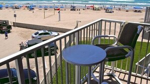 Een balkon met uitzicht op een strand, een tafel en stoelen.