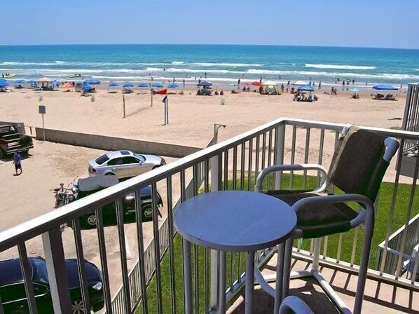 A balcony with a view of a beach, a table, and chairs.